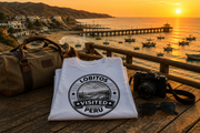 Gefaltetes Visited Lobitos T-Shirt mit Reisetasche und Kamera vor der Küste von Lobitos